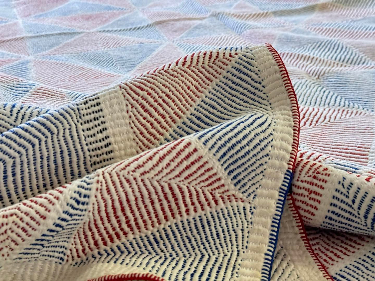 A close-up of a woven textile with a geometric pattern in cream, red, and blue, folded to show its texture and stitching.