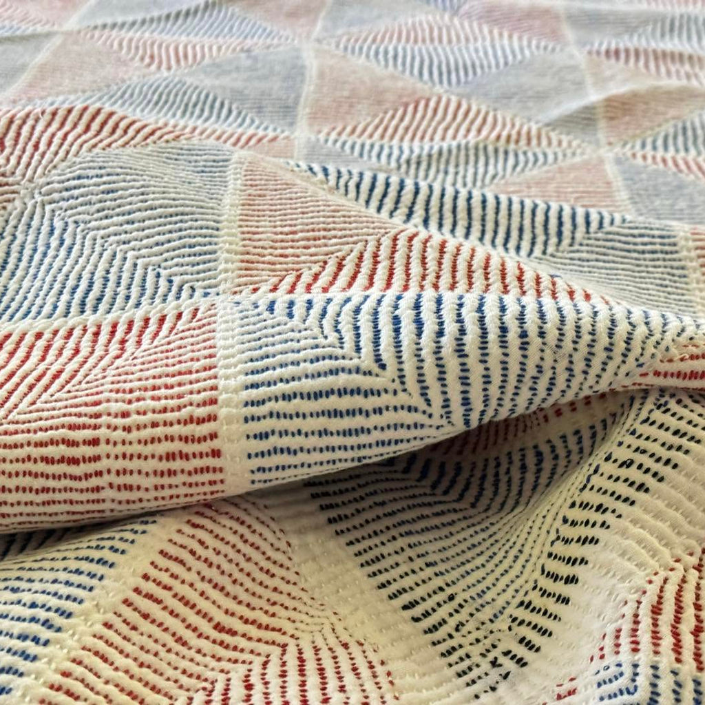 A close-up of a textured woven fabric with a geometric pattern in cream, blue, and rust red.
