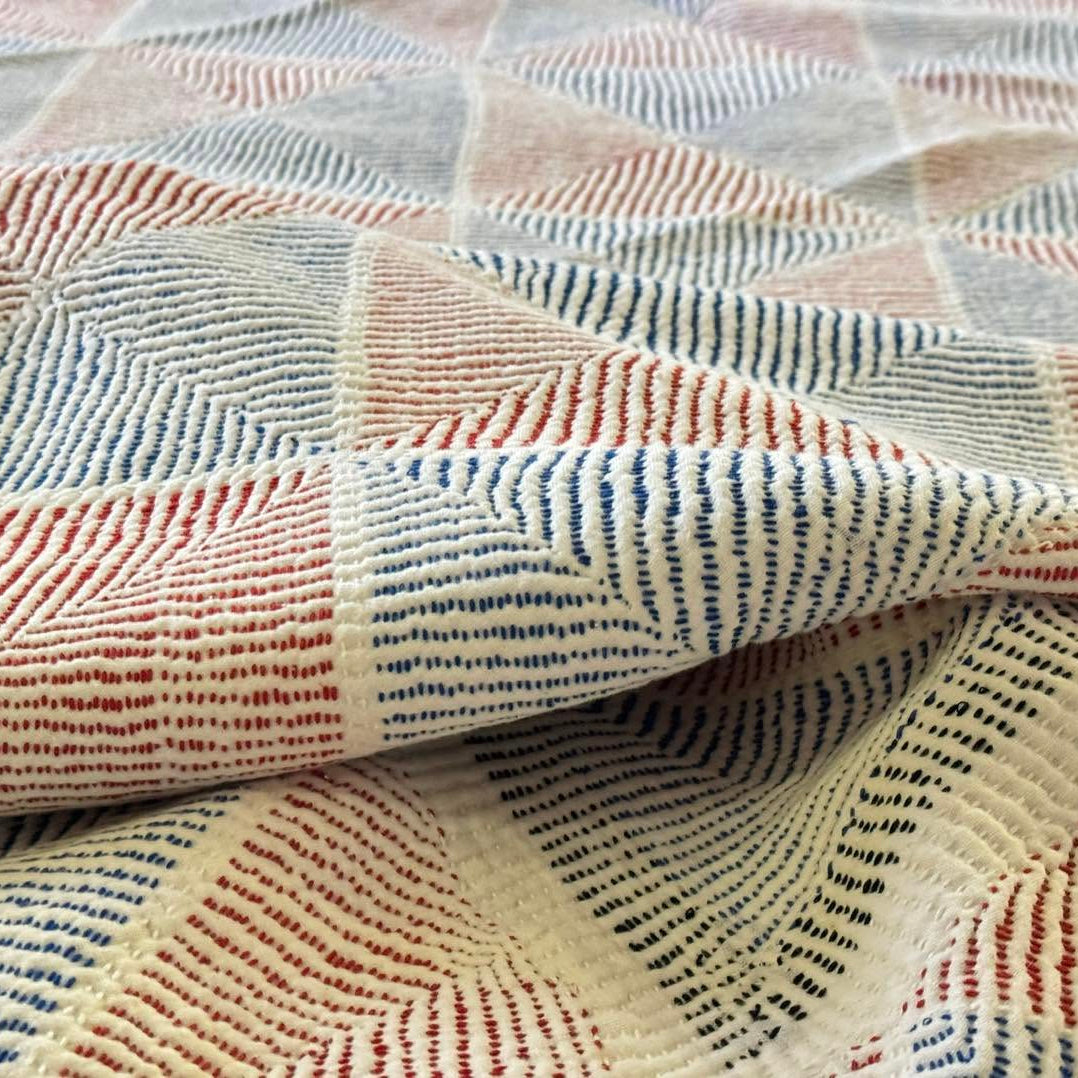 A close-up of a textured woven fabric with a geometric pattern in cream, blue, and rust red.