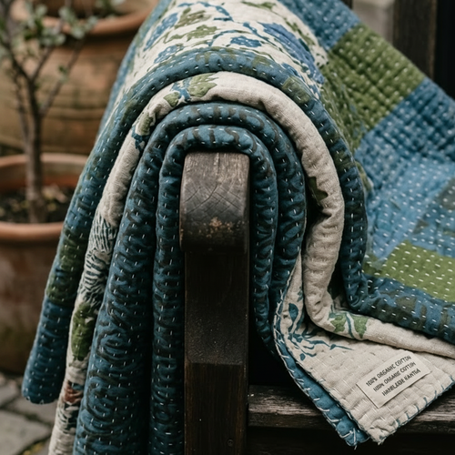 Rolled-up quilt with a floral pattern draped over a wooden chair outdoors.