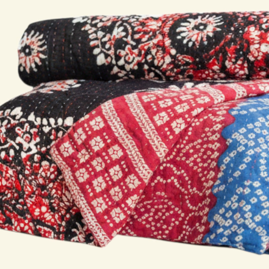 Two folded patterned quilts on a beige background