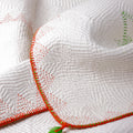 Close-up of a textured white fabric with orange trim and green accents on a white background