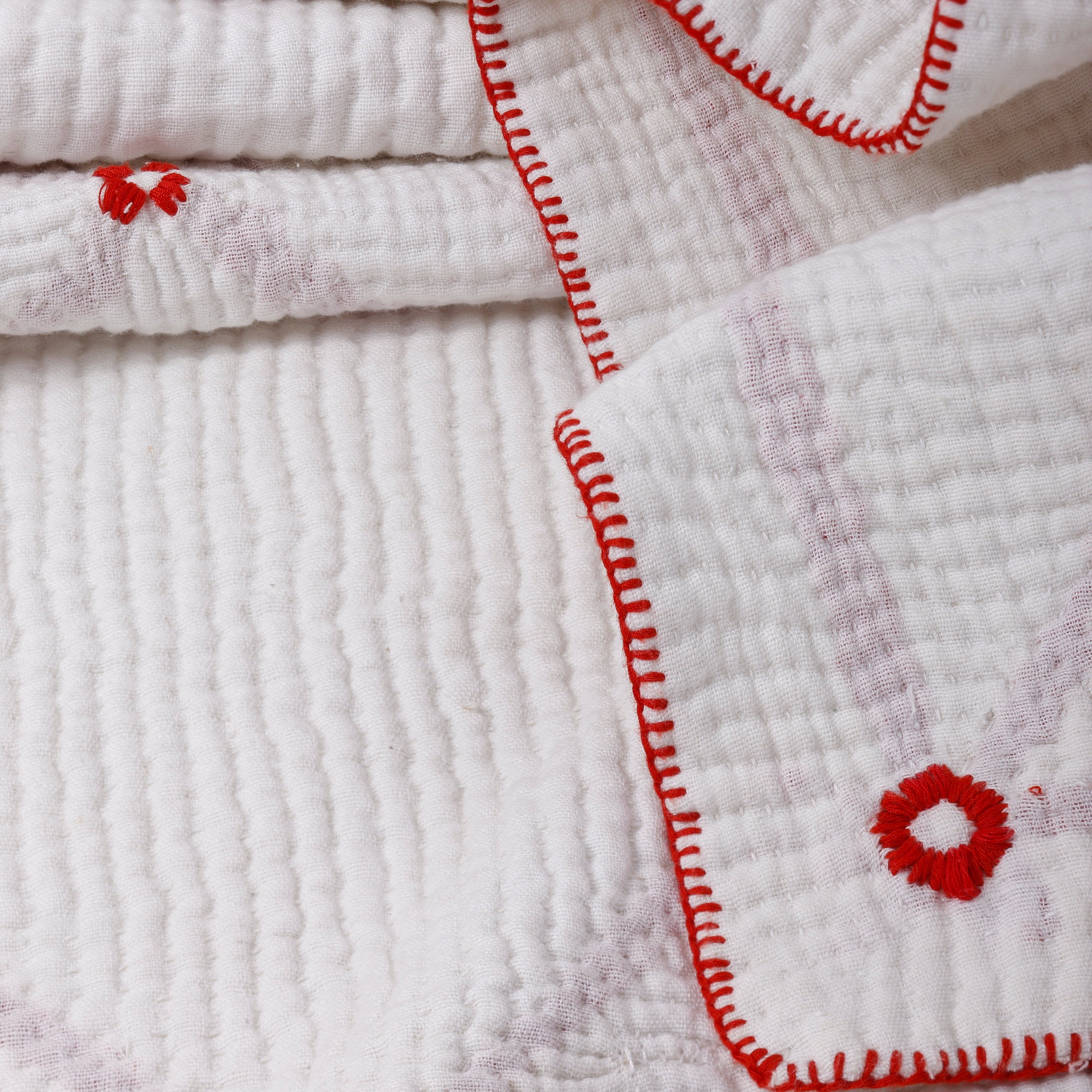 Stack of white textured towels with red floral embroidery on a neutral background