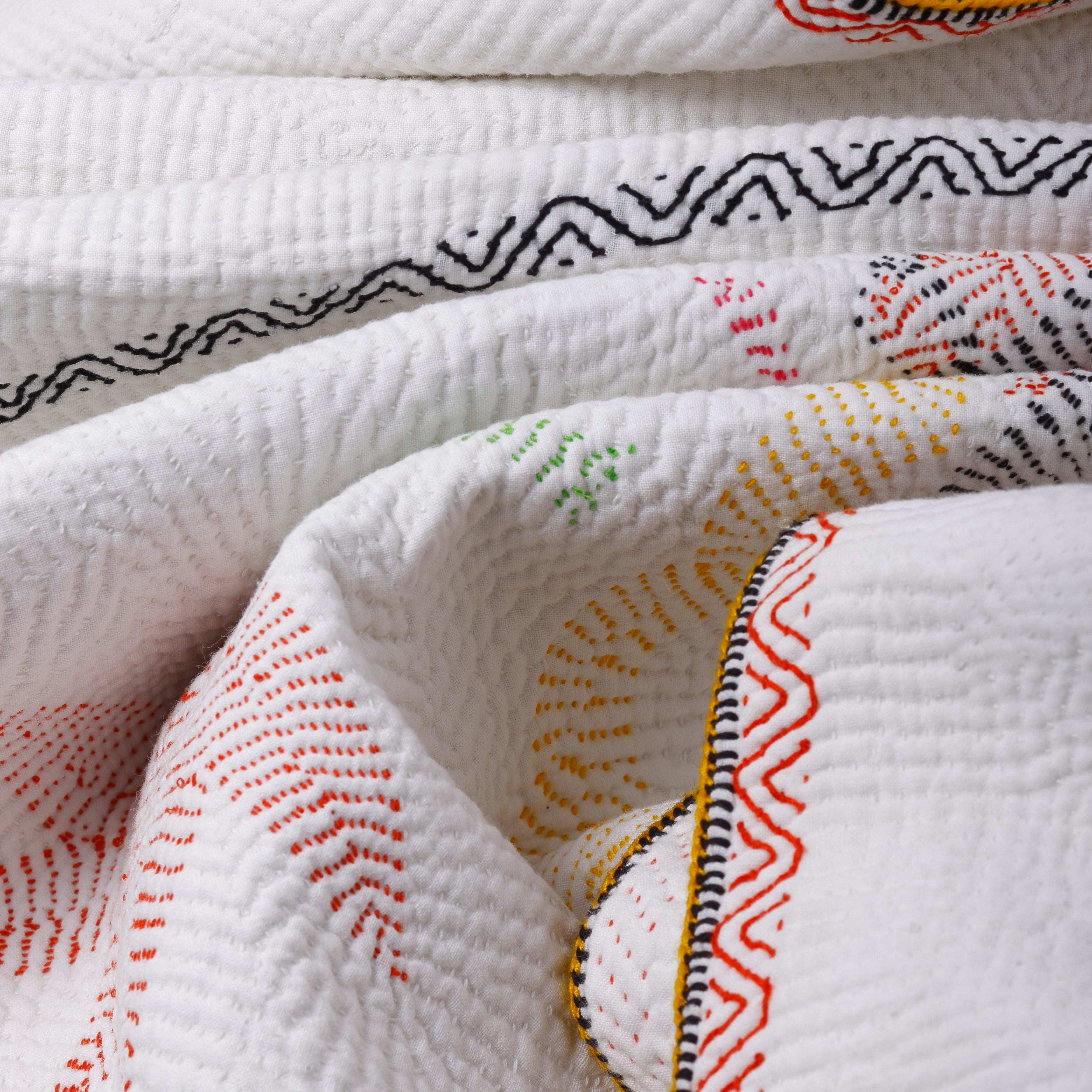 Close-up of a textured white fabric with colorful embroidery on a light gray background
