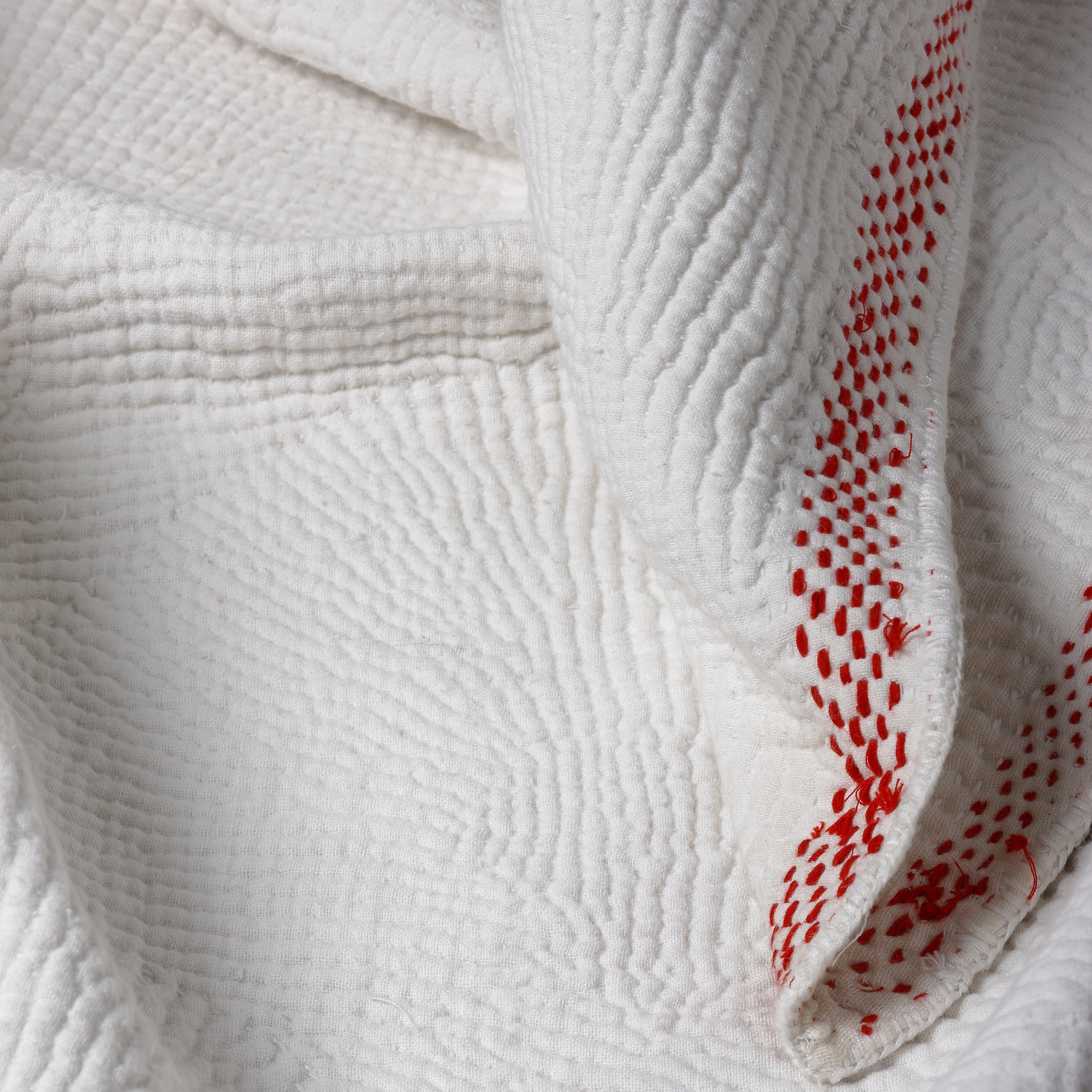 Close-up of textured white fabric with red stitching detail